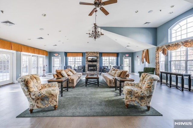 living room with ceiling fan with notable chandelier, hardwood / wood-style floors, and a stone fireplace