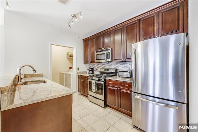 kitchen featuring light stone countertops, washer and clothes dryer, appliances with stainless steel finishes, tasteful backsplash, and sink