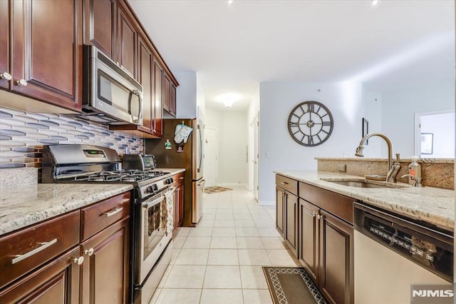 kitchen with light tile patterned floors, appliances with stainless steel finishes, decorative backsplash, light stone counters, and sink