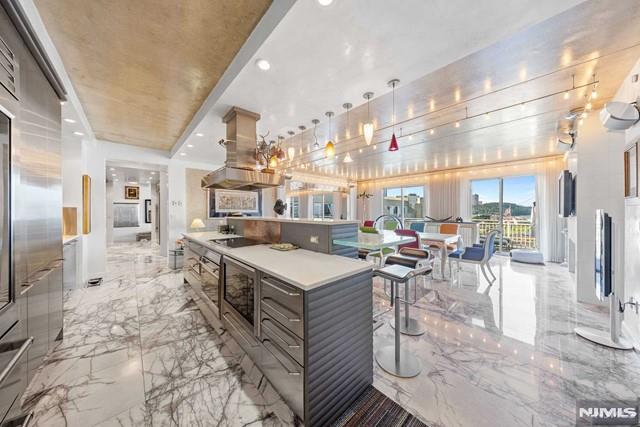 kitchen with pendant lighting, an island with sink, island exhaust hood, black electric cooktop, and a kitchen breakfast bar