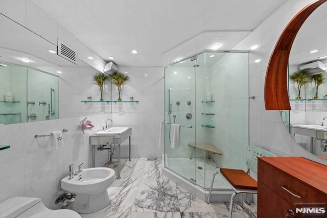 bathroom with tile walls, a shower with door, and a bidet