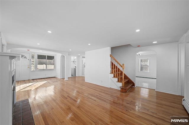 unfurnished living room featuring wood-type flooring, baseboard heating, and washer / dryer