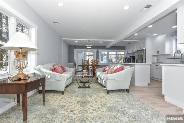 living room featuring beamed ceiling, sink, and light wood-type flooring