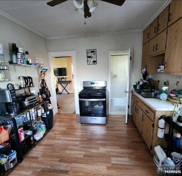 kitchen with gas stove, light hardwood / wood-style flooring, ornamental molding, and sink