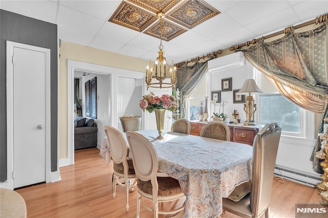 dining room featuring a paneled ceiling, light wood-type flooring, a wall unit AC, a baseboard heating unit, and an inviting chandelier