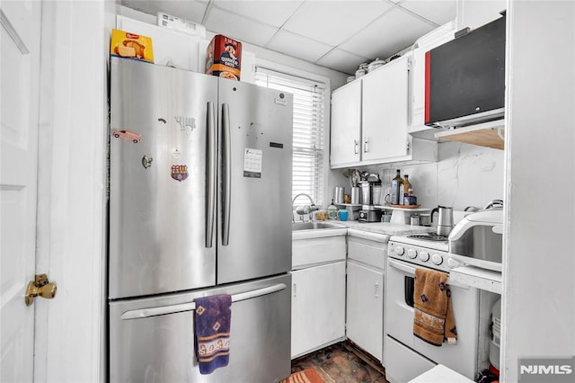 kitchen with backsplash, white range with gas stovetop, sink, stainless steel fridge, and white cabinetry