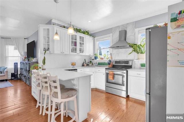 kitchen with a wealth of natural light, white cabinetry, stainless steel appliances, wall chimney range hood, and pendant lighting