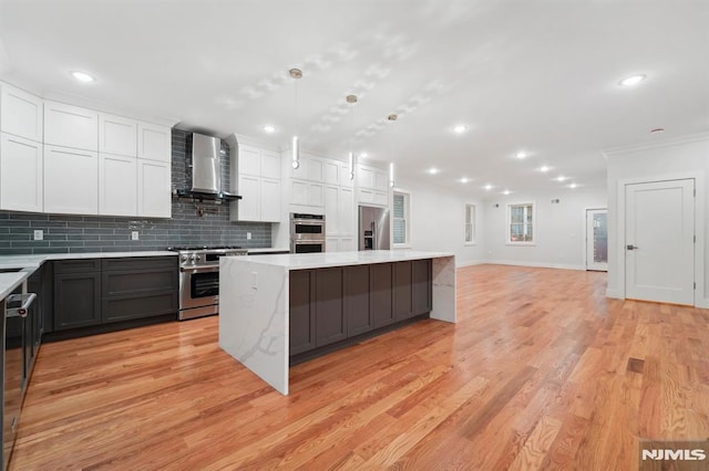 kitchen with wall chimney exhaust hood, pendant lighting, a center island, premium appliances, and white cabinets