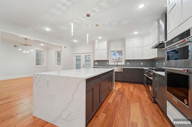 kitchen with appliances with stainless steel finishes, pendant lighting, wall chimney exhaust hood, a spacious island, and white cabinetry