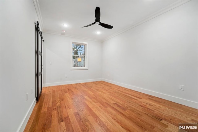 empty room featuring ceiling fan, a barn door, crown molding, and light hardwood / wood-style flooring