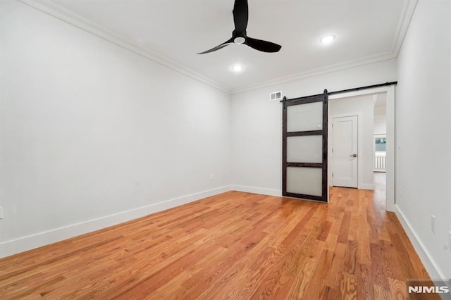 spare room featuring light wood-type flooring, ceiling fan, a barn door, and crown molding