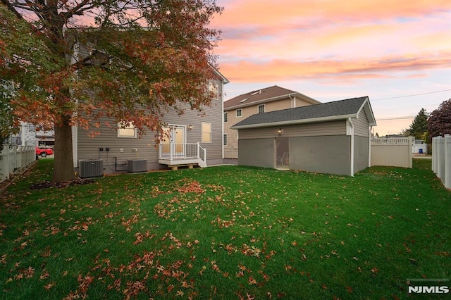 back house at dusk with a yard and central air condition unit