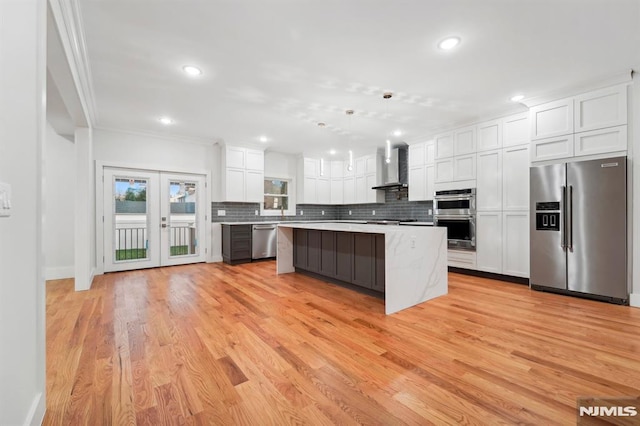 kitchen with wall chimney exhaust hood, a center island, decorative light fixtures, stainless steel appliances, and white cabinetry