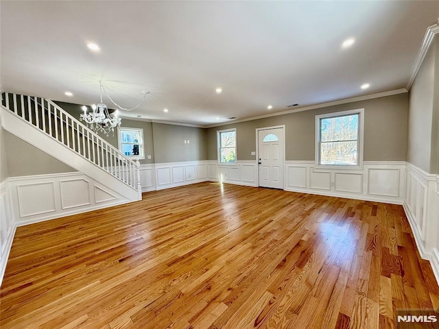 unfurnished living room featuring light hardwood / wood-style floors, an inviting chandelier, plenty of natural light, and ornamental molding