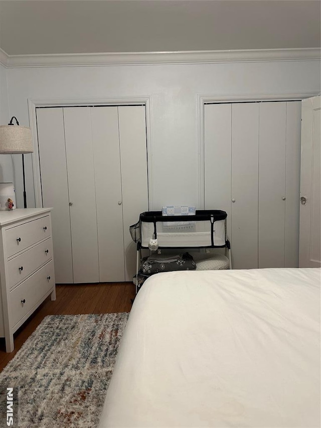 bedroom with two closets, crown molding, and dark hardwood / wood-style floors