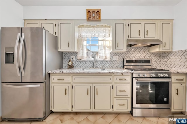 kitchen with sink, appliances with stainless steel finishes, backsplash, light stone countertops, and cream cabinetry