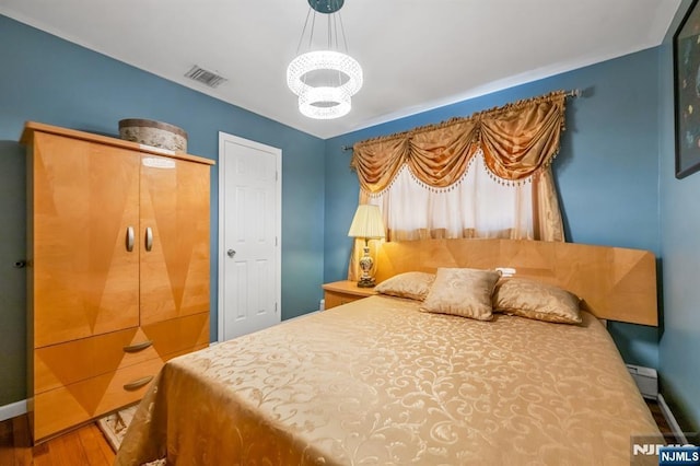 bedroom featuring hardwood / wood-style floors, a notable chandelier, and a baseboard heating unit