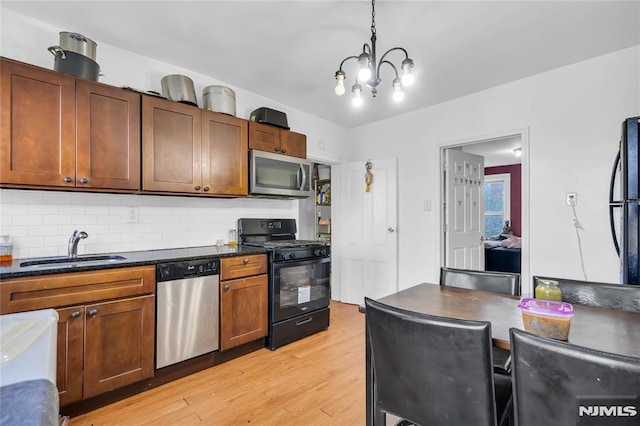 kitchen featuring sink, a notable chandelier, backsplash, pendant lighting, and black appliances