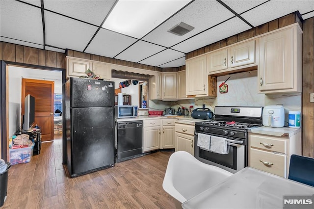 kitchen with cream cabinets, light wood-type flooring, a drop ceiling, and black appliances