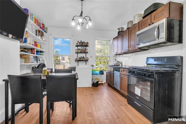 kitchen featuring pendant lighting, backsplash, light wood-type flooring, a notable chandelier, and stainless steel appliances