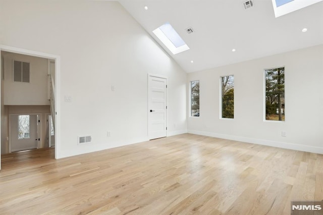 empty room featuring high vaulted ceiling, a skylight, and light wood-type flooring