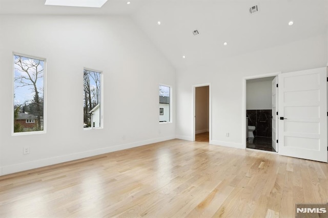 unfurnished living room with high vaulted ceiling, a skylight, and light hardwood / wood-style flooring