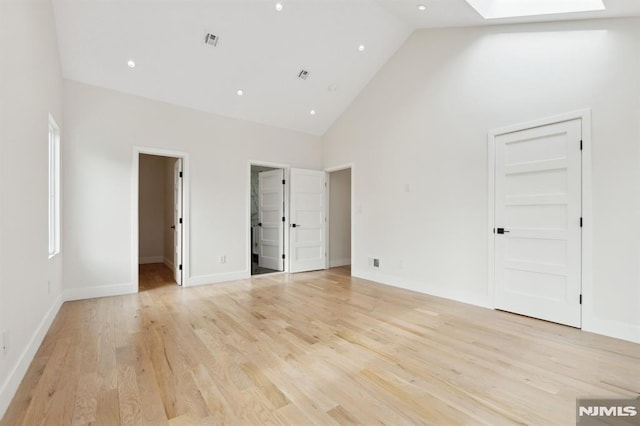 unfurnished bedroom featuring ensuite bathroom, a skylight, light wood-type flooring, high vaulted ceiling, and a walk in closet