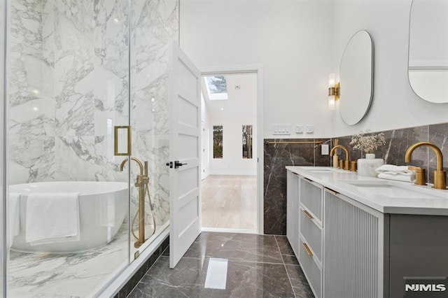 bathroom with tile walls, vanity, a skylight, and a bathing tub