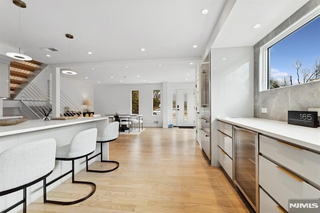 kitchen with light hardwood / wood-style floors, wine cooler, white cabinets, and hanging light fixtures