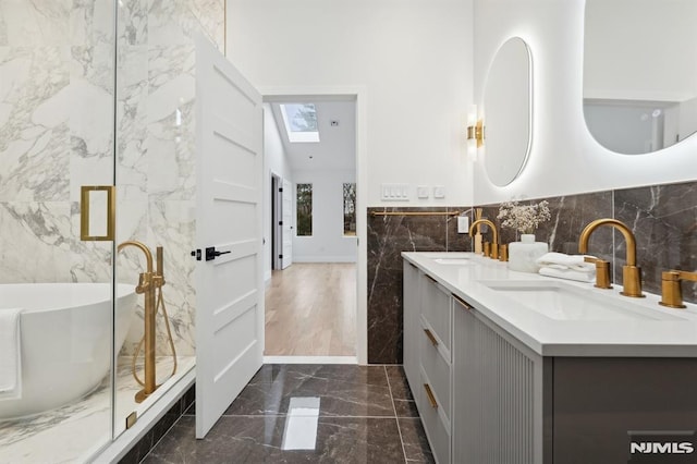 bathroom featuring vaulted ceiling with skylight, a washtub, vanity, and tile walls