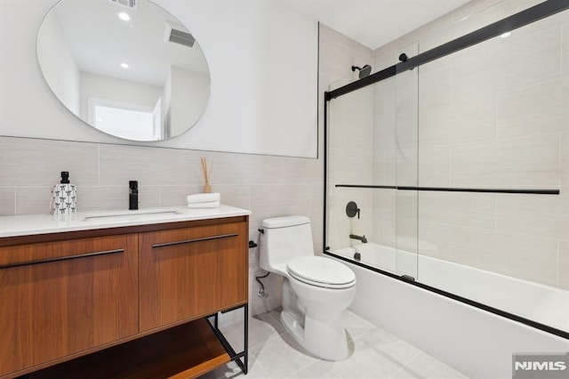 full bathroom featuring toilet, combined bath / shower with glass door, tile walls, tile patterned floors, and vanity