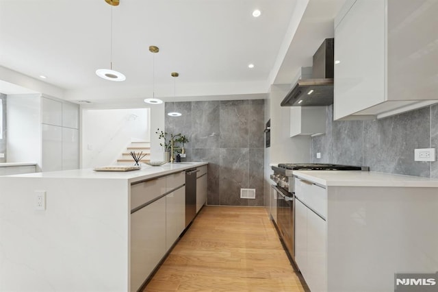 kitchen featuring white cabinets, wall chimney exhaust hood, decorative light fixtures, stainless steel appliances, and light hardwood / wood-style flooring