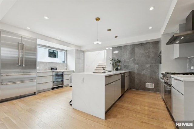 kitchen featuring light hardwood / wood-style floors, decorative light fixtures, wine cooler, wall chimney range hood, and high end appliances