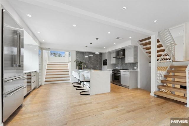 kitchen featuring premium appliances, a center island, wall chimney range hood, light hardwood / wood-style floors, and a breakfast bar area