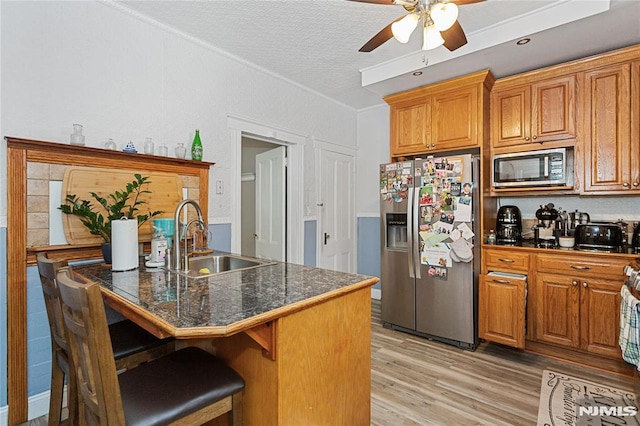 kitchen with a breakfast bar area, appliances with stainless steel finishes, ceiling fan, sink, and light hardwood / wood-style flooring