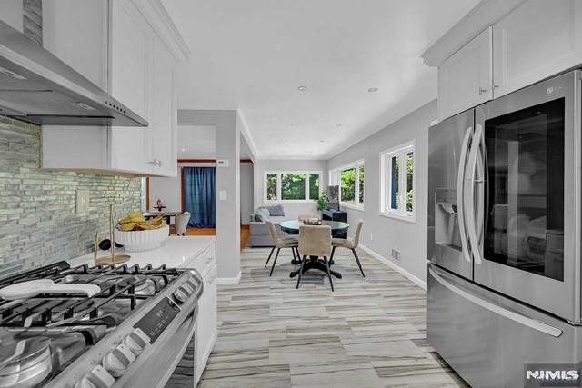 kitchen featuring tasteful backsplash, white cabinets, wall chimney exhaust hood, and stainless steel appliances