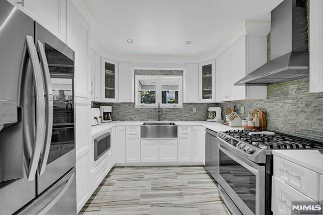 kitchen with white cabinets, wall chimney range hood, sink, decorative backsplash, and stainless steel appliances