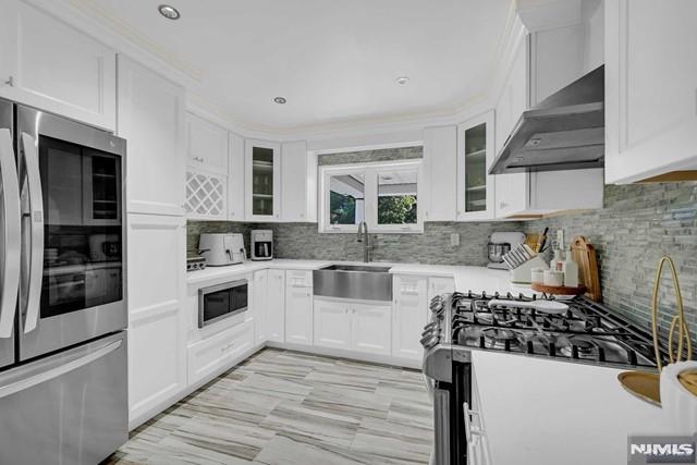 kitchen with wall chimney range hood, sink, stainless steel fridge, gas stove, and white cabinetry