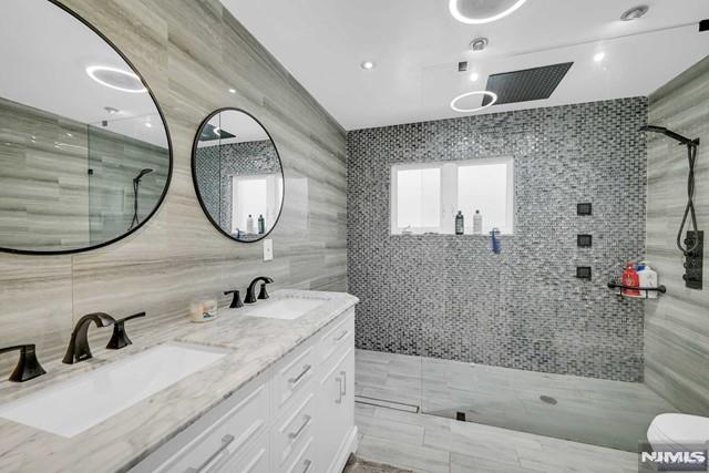 bathroom with vanity, a tile shower, and tile walls