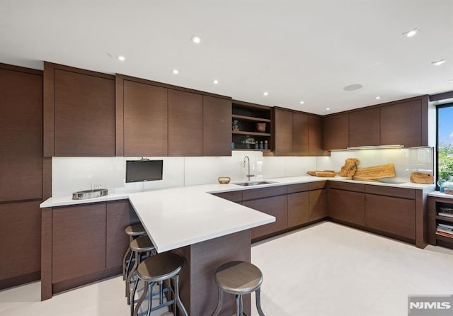 kitchen with kitchen peninsula, dark brown cabinets, a kitchen breakfast bar, and sink