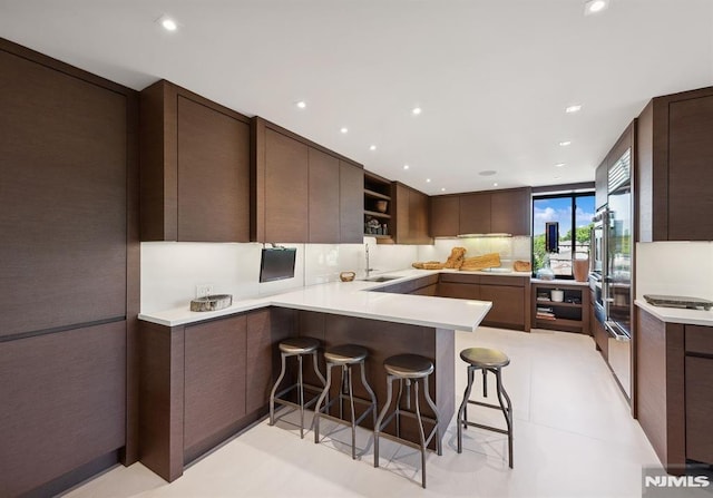 kitchen with a breakfast bar, sink, light tile patterned floors, dark brown cabinets, and kitchen peninsula