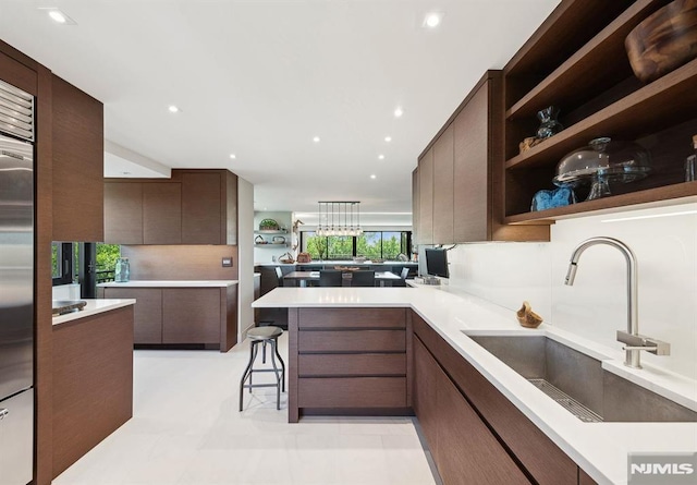 kitchen with kitchen peninsula, high end fridge, dark brown cabinetry, sink, and a breakfast bar area