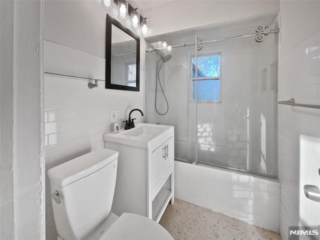 full bathroom featuring toilet, tile walls, vanity, and shower / bath combination with glass door