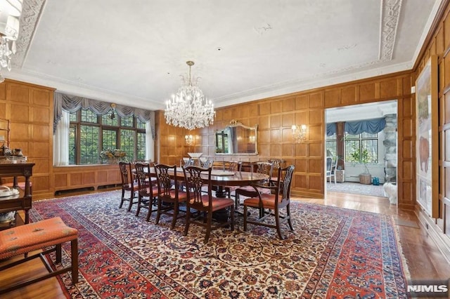 dining space with crown molding, hardwood / wood-style flooring, wood walls, and a notable chandelier