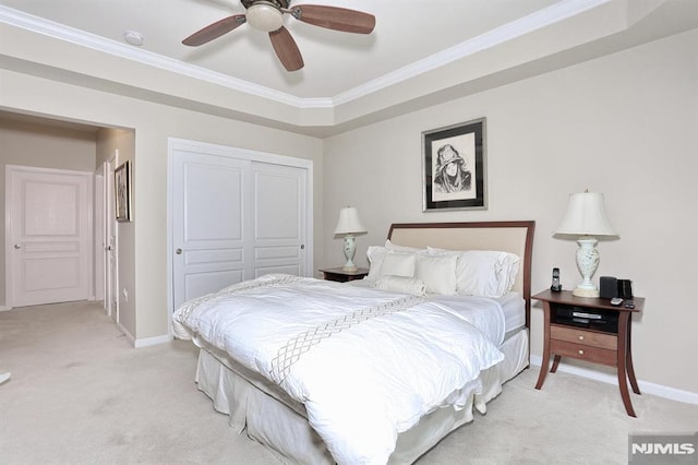 bedroom with ceiling fan, crown molding, light colored carpet, a tray ceiling, and a closet