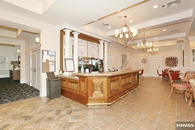 bar with light stone countertops, decorative light fixtures, decorative columns, and a notable chandelier