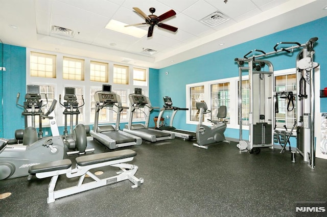 gym featuring a paneled ceiling, ceiling fan, and a raised ceiling