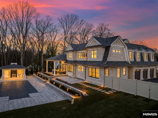 back house at dusk with an outbuilding, a patio, and a lawn