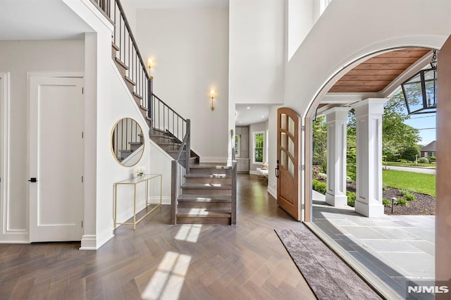 entrance foyer featuring decorative columns, dark parquet flooring, plenty of natural light, and a high ceiling