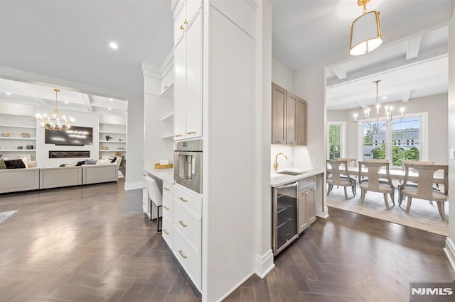 kitchen featuring an inviting chandelier, sink, wine cooler, beamed ceiling, and white cabinetry